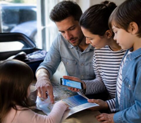 Gezin dat vakanties vergelijkt met vakantiegids en telefoon aan een bureau bij een raam